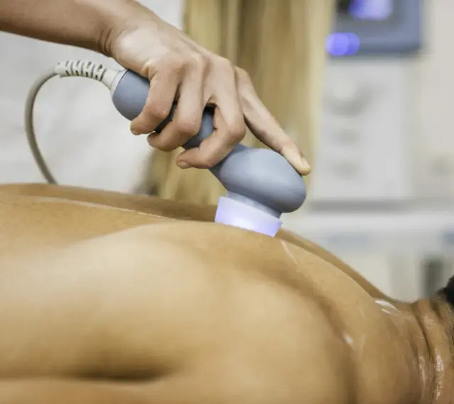Physiotherapeutin behandelt Rückenschmerzen mit Ultraschall. Die Behandlung lindert Schmerzen nach Verletzungen.