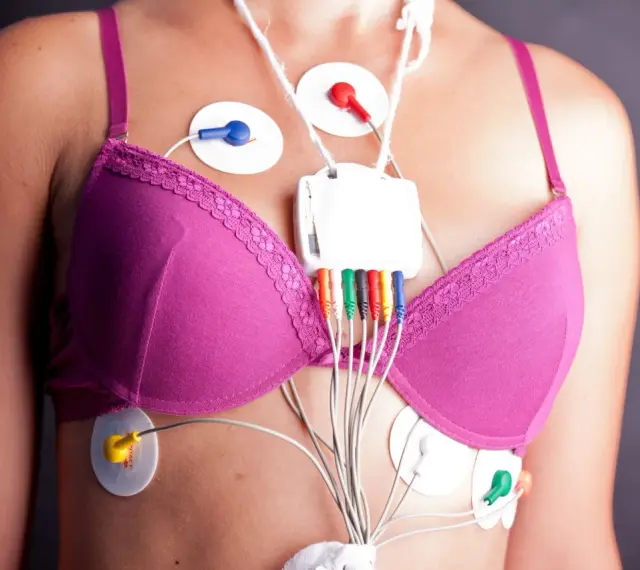 Kobieta w różowym biustonoszu z elektrodami EKG i rejestratorem Holtera na klatce piersiowej.