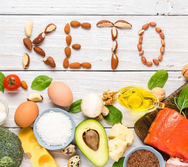 Słowa "KETO" ułożone z orzechów i nasion. Wokół składniki diety keto: ryba, mięso, jajka, awokado, olej, ser, warzywa.