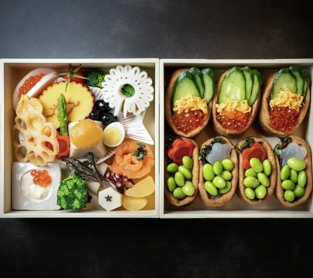 Dwa pudełka z japońskimi przysmakami: jedno z różnorodnymi składnikami, drugie z inari sushi na słodko, wypełnione edamame i ikrą.