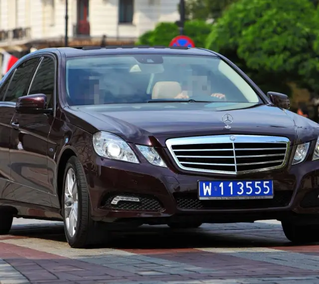 Ciemnobrązowy Mercedes z tablicą W 113555, wskazującą na rejestracje dyplomatyczne.