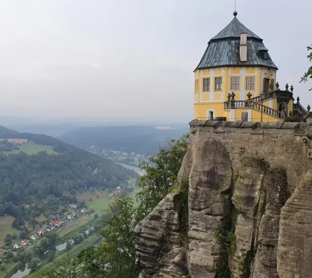 Żółty pałac na skale, część twierdzy Königstein, góruje nad doliną rzeki i lasami.