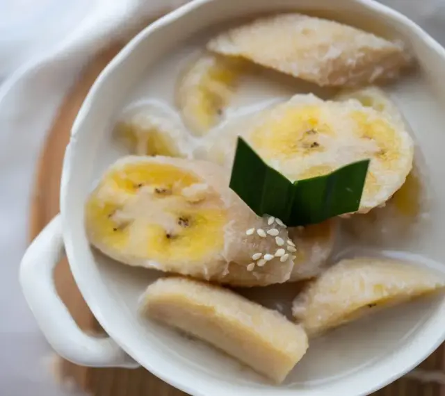 Kawałki banana w mleku kokosowym, ozdobione liściem pandanu i sezamem. Pyszny tajski deser.