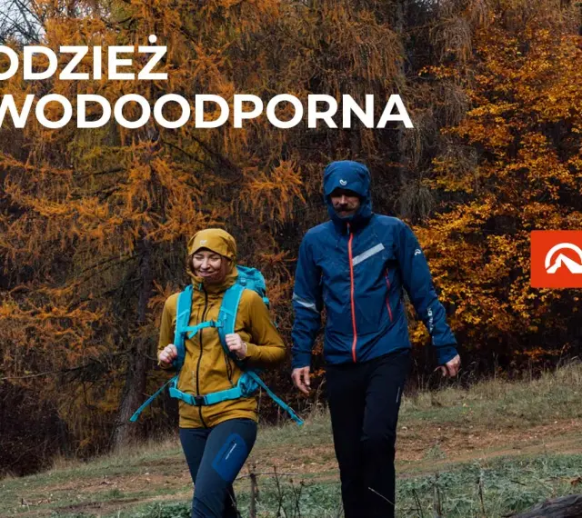 Para idzie przez jesienny las w odzieży wodoodpornej. To oferta firmy Northfinder, która specjalizuje się w odzieży outdoorowej.