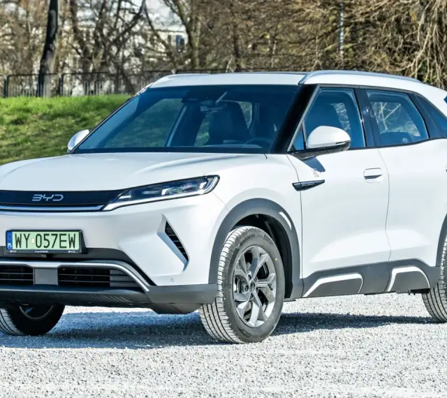 Biały SUV z logo BYD, jeden z chińskich samochodów elektrycznych, zaparkowany na żwirowej nawierzchni.