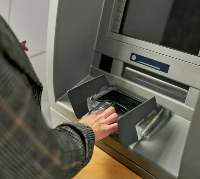 Dłoń w rękawie w kratę wkłada pieniądze do bankomatu. Szybka jednorazowa wpłata gotówki do banku.