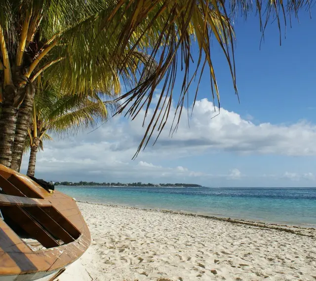 Mauritius pora deszczowa. Drewniana łódź na piaszczystej plaży pod palmami, turkusowe morze i błękitne niebo z chmurami.