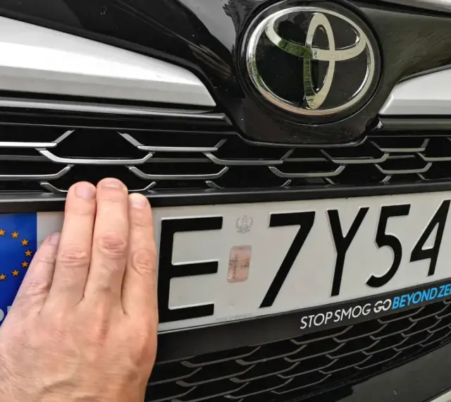 Dłoń zasłania część tablicy rejestracyjnej E 7Y541. Pod nią widoczny jest napis "STOP SMOG GO BEYOND ZERO".