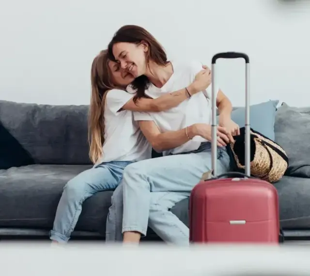 Mama i córka przytulają się na kanapie, obok walizka. Wszyscy, którzy chcą zameldować się w hotelu, mogą tu poczuć się jak w domu.