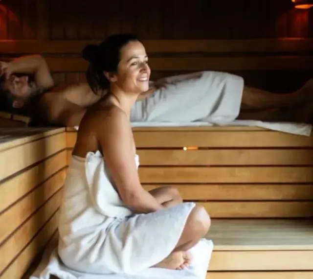 Para relaksu w saunie. Kobieta w ciąży i mężczyzna odpoczywają w drewnianej saunie, otuleni ręcznikami.