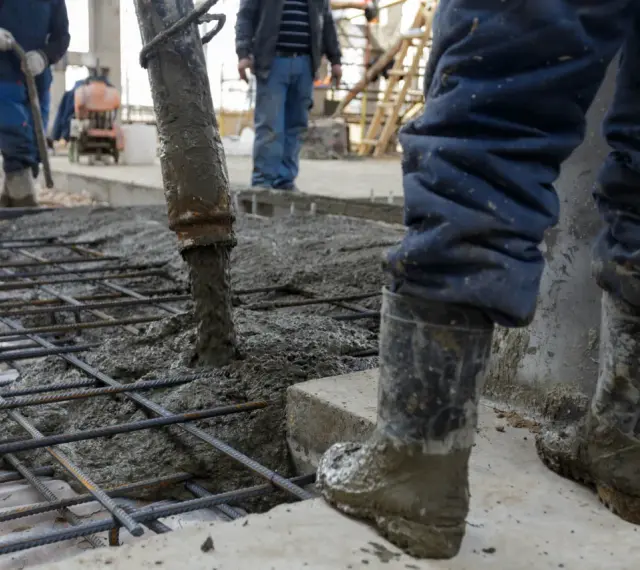 Beton wylewany na zbrojenie. Pracownicy w gumowcach nadzorują proces, który decyduje, ile kosztują fundamenty.