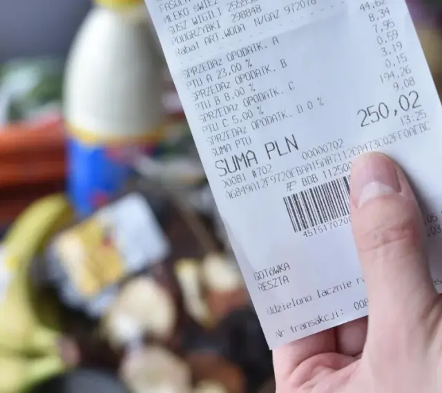 Ręka trzyma paragon z zakupów spożywczych, na którym widnieje suma 250,02 zł. Zastanawiasz się, gdzie wyrzucać paragony? Ten jest z papieru termicznego.