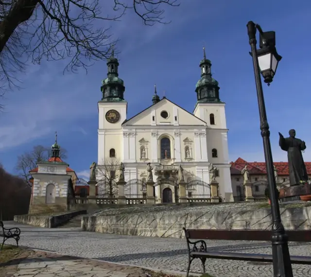 Kalwaria Zebrzydowska zwiedzanie: barokowy kościół z wieżami, kapliczki, ławki i pomnik.
