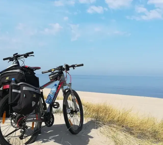 Dwa rowery z sakwami na plaży, gotowe na przygodę wzdłuż Velo Baltica. Morze i niebo tworzą tło.