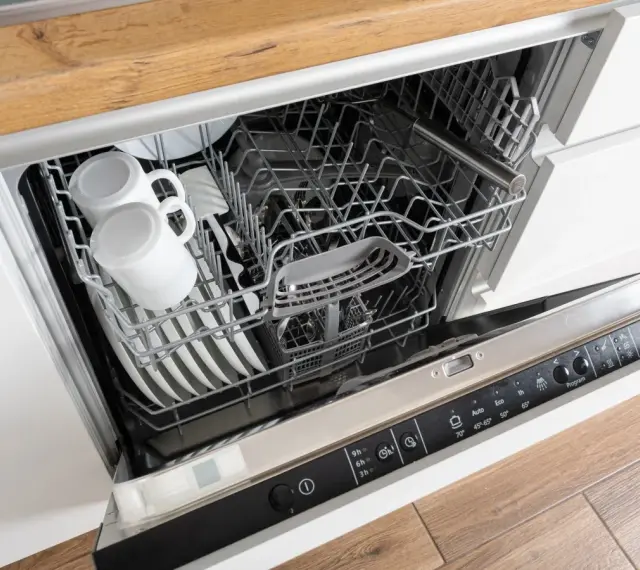 Wnętrze zmywarki Whirlpool 6th Sense z koszami pełnymi naczyń, w tym kubków i talerzy.