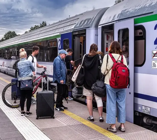 Ludzie z bagażami i rowerem czekają na pociąg PKP na peronie.