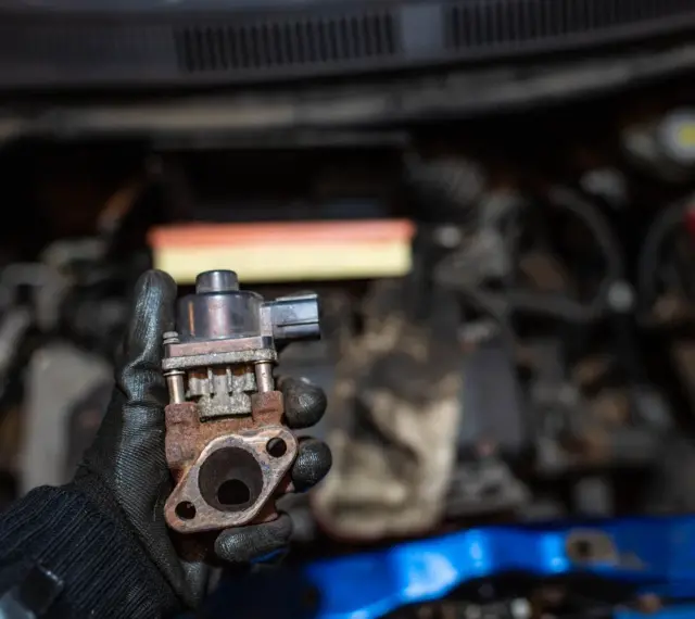 Zardzewiały zawór EGR w dłoni mechanika. Może to być przyczyna problemów z silnikiem, np. nierównej pracy.