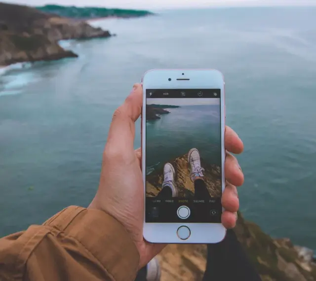 Dłoń trzyma iPhone'a 15, na ekranie widok klifów i oceanu. Czy iPhone 15 jest wodoszczelny? To pytanie zadaje sobie wielu podróżników.