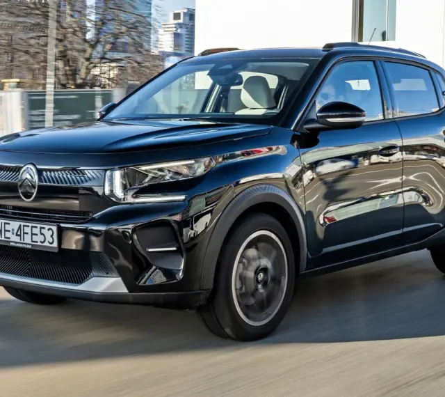 Czarny Citroen C3 porusza się po mieście, odbijając światła i budynki w swojej lśniącej karoserii.