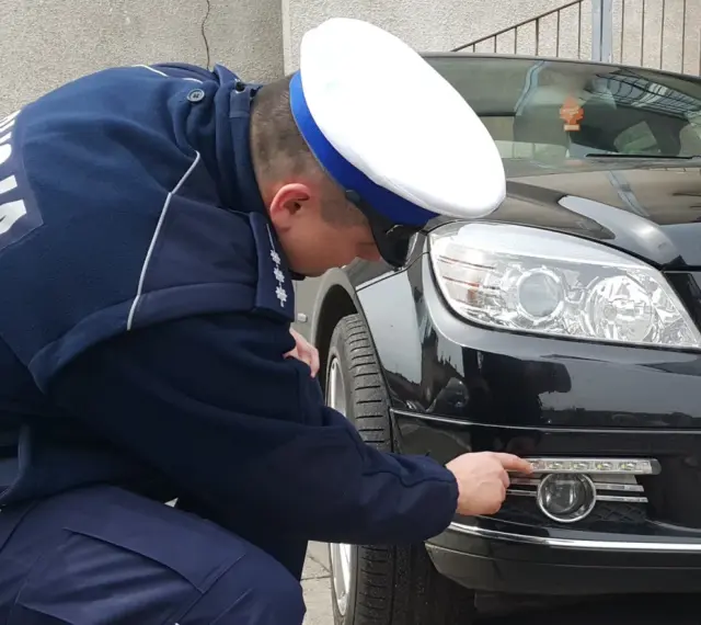 Policjant sprawdza, jakie światła do jazdy dziennej zamontowano w czarnym Mercedesie.