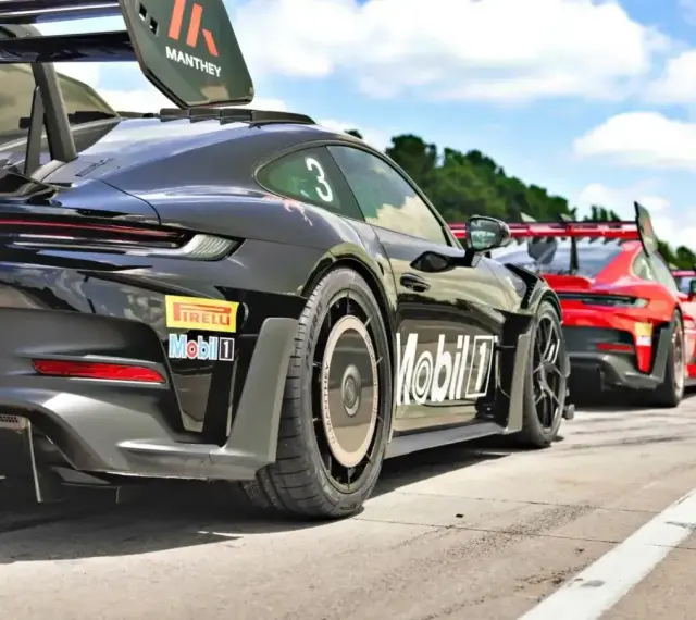Czarny Porsche GT3 RS z numerem 3 i logo Manthey na skrzydle, gotowy do wyścigu obok czerwonych samochodów.