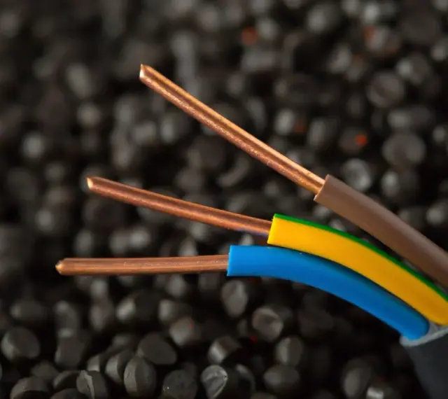 Trzy miedziane żyły kabla elektrycznego, w izolacjach brązowej, żółto-zielonej i niebieskiej, na tle granulatów tworzywa sztucznego. Idealne do instalacji IP20.
