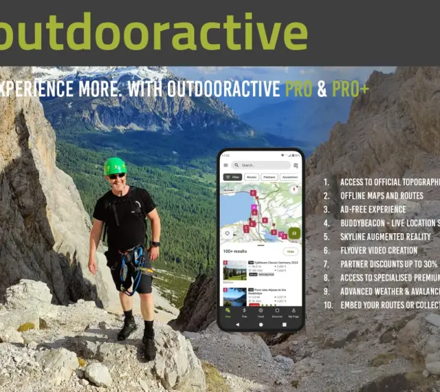Escursionista sorridente in montagna, con smartphone che mostra l'app outdooractive gratis con mappe e percorsi.