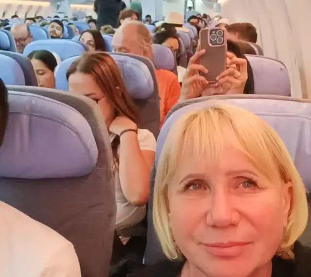 W samolocie, przygotowując się na najdłuższy lot samolotem, pasażerowie siedzą w rzędach. Kobieta robi zdjęcie telefonem.