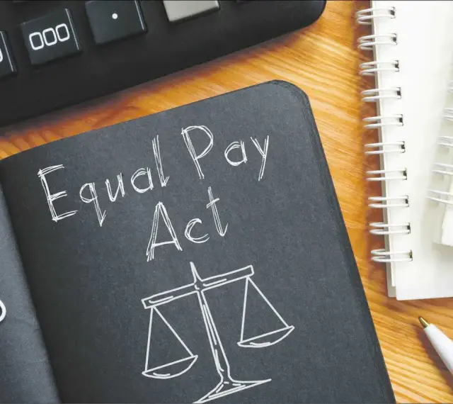 Notatnik z napisem "Equal Pay Act" i wagą sprawiedliwości symbolizuje jawność wynagrodzeń. Obok kalkulator i długopis.
