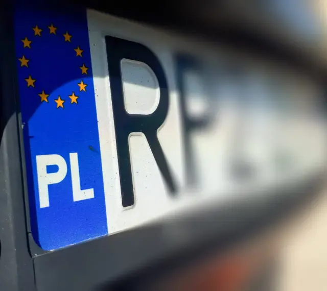 Zbliżenie na polską tablicę rejestracyjną z symbolem UE. Litery "PL" i fragment innych znaków sugerują, że pojazd jest w trakcie wyrejestrowania.