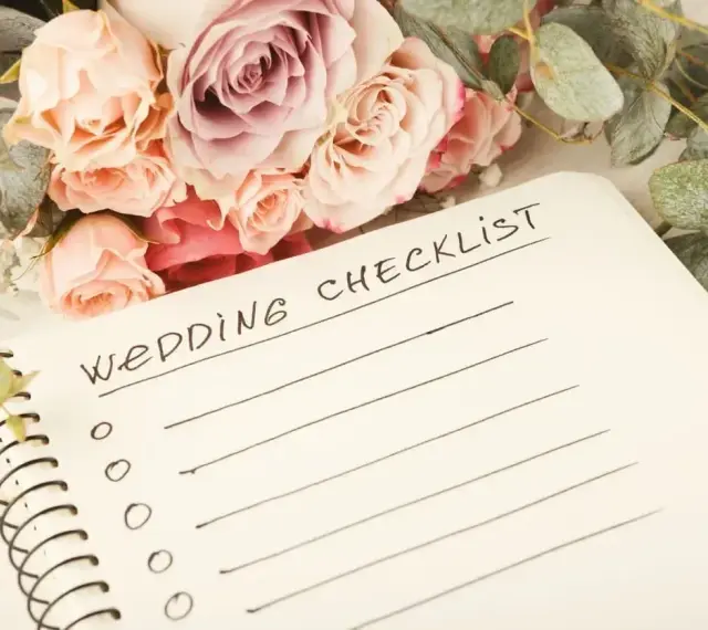 Bukiet róż i eukaliptusa obok notatnika z napisem "Wedding Checklist". Planowanie przebiegu wesela zaczyna się od listy zadań.