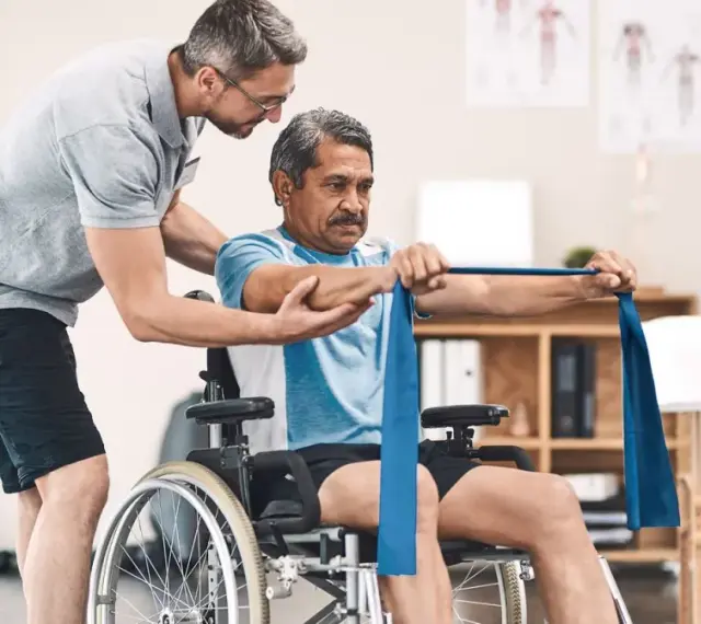 Ein Mann im Rollstuhl trainiert mit einem Therapeuten, der ihm hilft, die Widerstandsbandübungen auszuführen. Die Physiotherapeuten unterstützen ihn bei seiner Genesung.