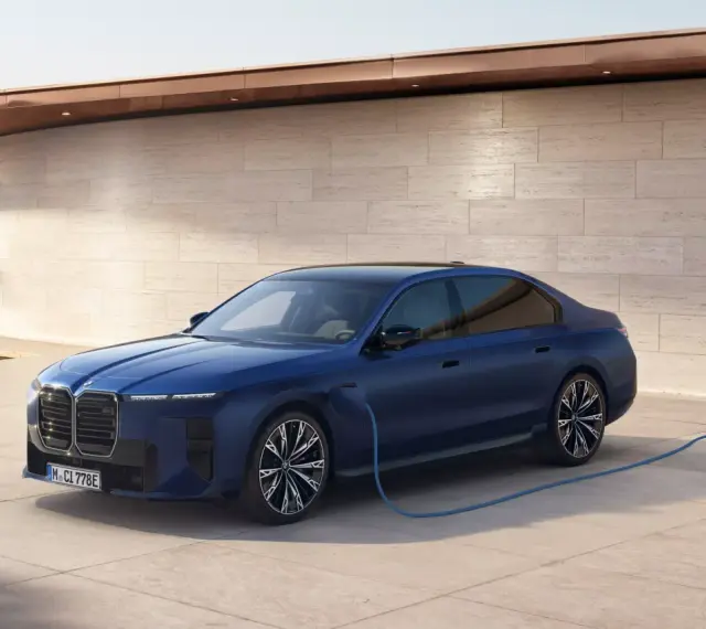 Elegancka, granatowa BMW hybryda podłączona do ładowarki przy nowoczesnym domu z widokiem na morze.