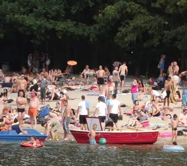 Tłum ludzi odpoczywa na plaży nad jeziorem w Jelczu Laskowicach. Słońce, piasek i woda tworzą idealne warunki do letniego relaksu.