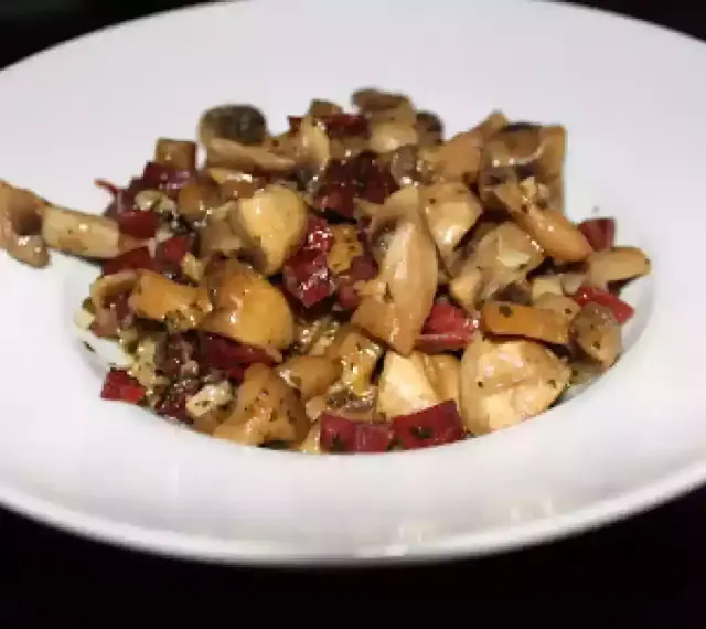 Champiñones salteados con trocitos de jamón, servidos en un plato blanco. Un plato sencillo y sabroso.