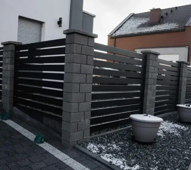 Nowoczesne ogrodzenie z betonowych słupków i ciemnych paneli. Taka wysokość ogrodzenia bez pozwolenia zapewnia prywatność.