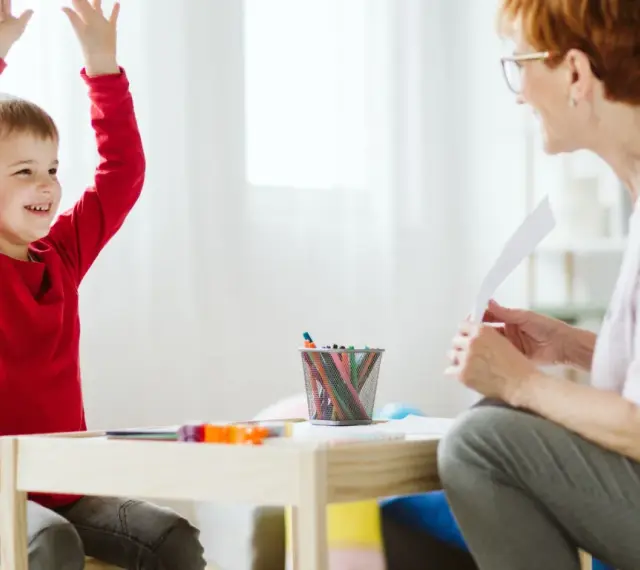 Chłopiec z podniesionymi rękami, uśmiechnięty, podczas sesji terapeutycznej. Może to być pomocne w ocenie objawów ADHD u dzieci test.