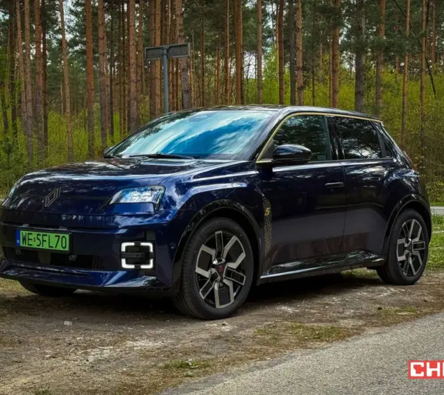 Ciemnoniebieski Renault 5 E-Tech elektryczny stoi na drodze leśnej.