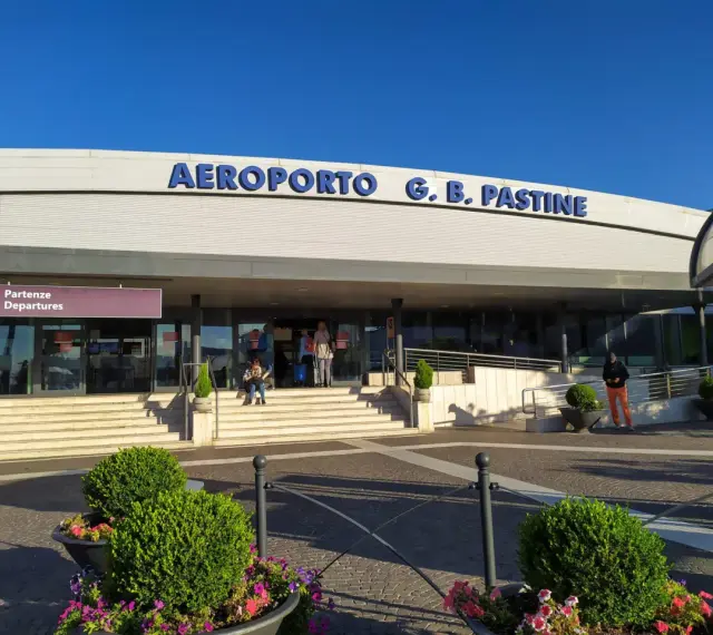 Wejście do Aeroportu G.B. Pastine w Rzymie Ciampino. Słoneczny dzień, ludzie czekają na odloty.