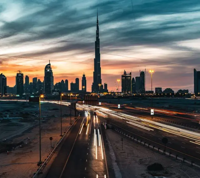 Wieczorny widok na Dubaj z Burj Khalifa, gdzie światła samochodów tworzą smugi na autostradzie. Ciekawostki o tym drapaczu chmur mogą dotyczyć jego wysokości i budowy.