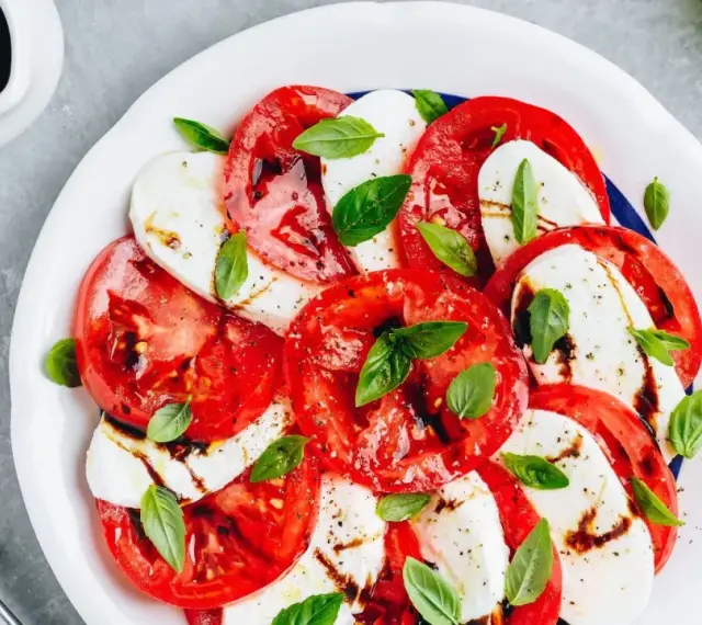 Pyszna sałatka caprese z pomidorów, mozzarelli i bazylii, polana sosem balsamicznym.