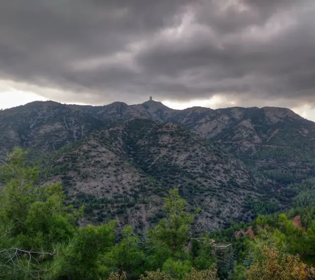 Góry Troodos pod burzliwym niebem. W oddali na szczycie widać charakterystyczną budowlę.