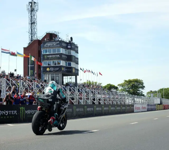 Motocyklista ściga się na wyspie Man, mijając trybuny pełne widzów i wieżę kontrolną.