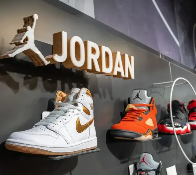Na wystawie butów Jordan, białe Air Jordan 1 z złotymi akcentami. Obok pomarańczowe Air Jordan 5. Czy 8 5 jaki to rozmiar buta?