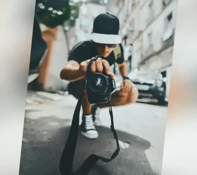 Młody fotograf w czapce z daszkiem trzyma aparat, zastanawiając się, ile zarabia fotograf w dzisiejszych czasach.
