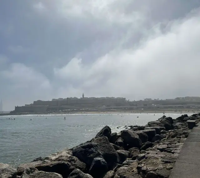 Spokojna plaża z surferami i miastem w tle. Czy Maroko jest bezpiecznym krajem? Widok sugeruje, że tak, ludzie cieszą się słońcem i morzem.