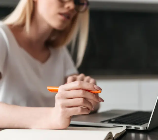 Kobieta pisze przykładowe uzasadnienie wniosku o przyznanie pomocy zdrowotnej na okulary, korzystając z laptopa i notatnika.