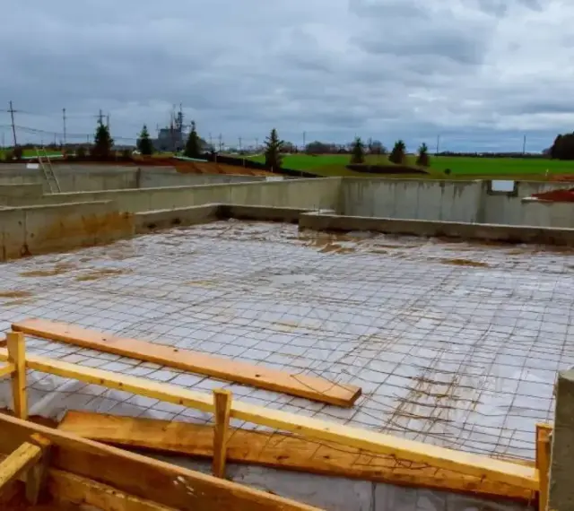 Fundament budowlany z zbrojeniem, przygotowany pod wylanie betonu. Widać betonowe ściany fundamentowe i siatkę stalową na podłożu.
