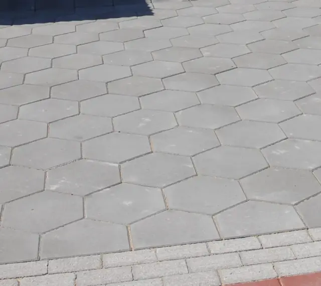 Szara, sześciokątna trelinka tworzy wzór na chodniku.