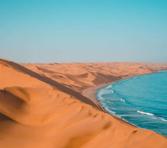 Piaskowe wydmy Namibii spotykają się z turkusowym oceanem. Idealna namibia pogoda na podziwianie tego kontrastu.